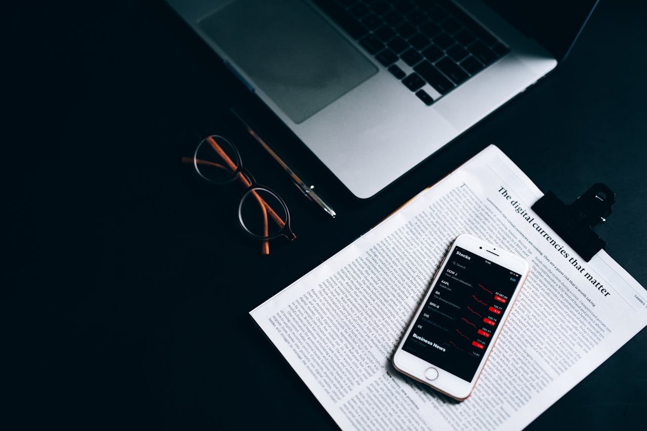 our-experience Flat lay of a digital workspace featuring a smartphone, glasses, and a laptop on a dark desk.