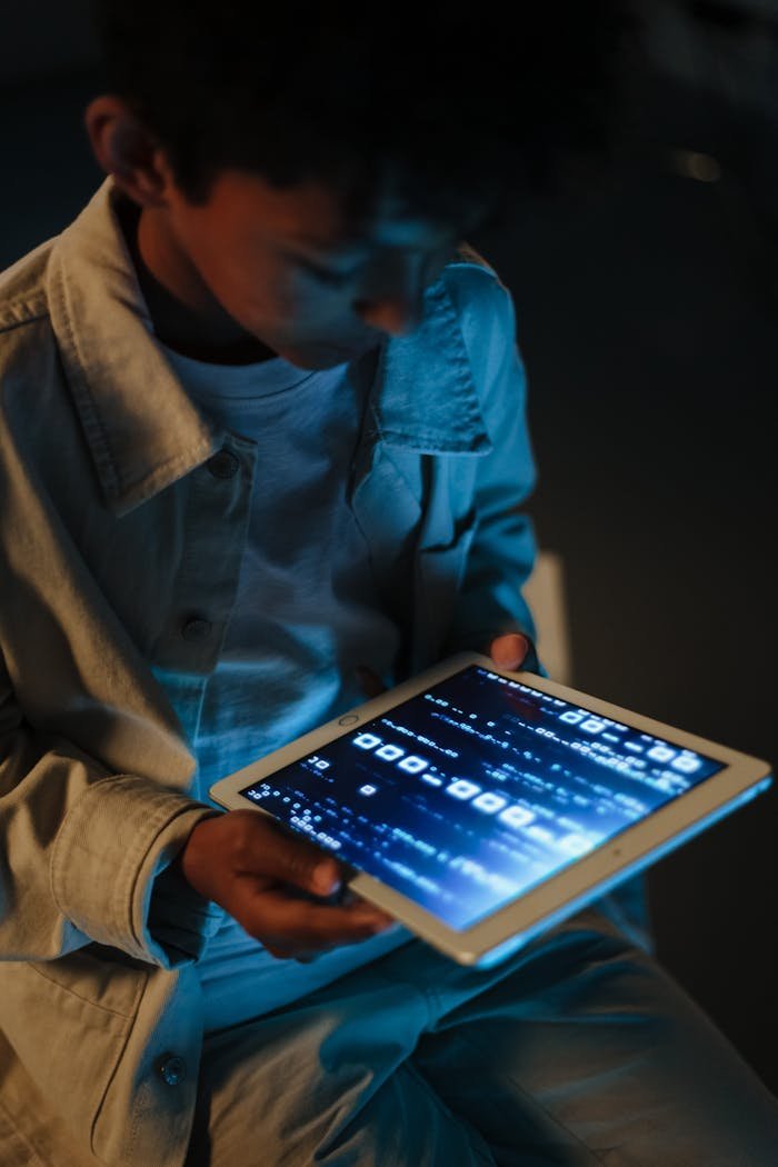 about-img A child engrossed in using a digital tablet at night, illuminated by screen light.